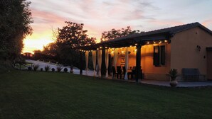 Una casa con un patio coperto, un prato e un tramonto sullo sfondo.