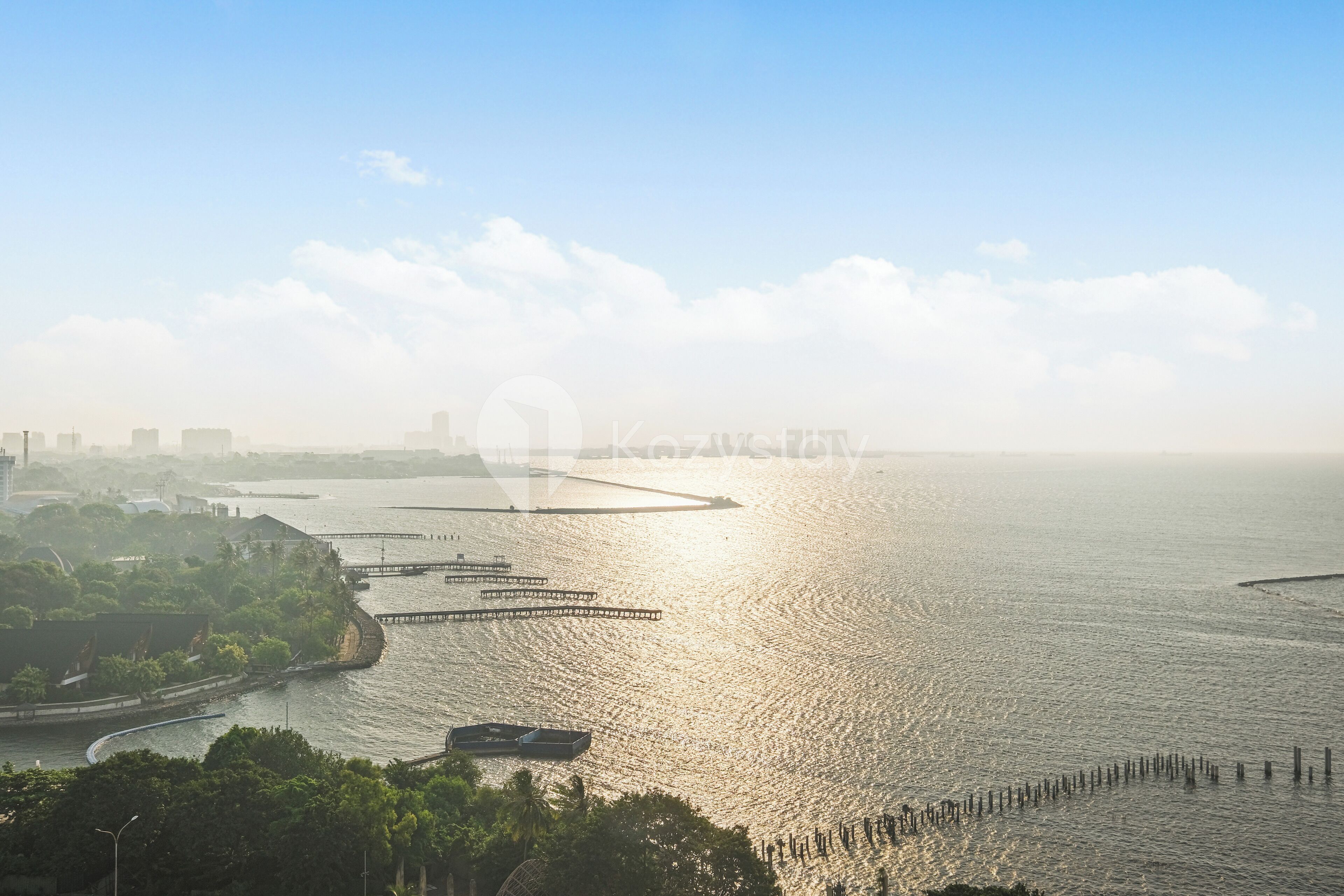A coastal cityscape with a marina, boats, and a pier extending into the water.
