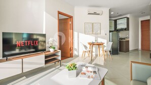 Ein modernes Wohnzimmer mit Flachbildfernseher, Couchtisch mit Zeitschrift, Zimmerpflanze und Essbereich mit Stühlen und Tisch.