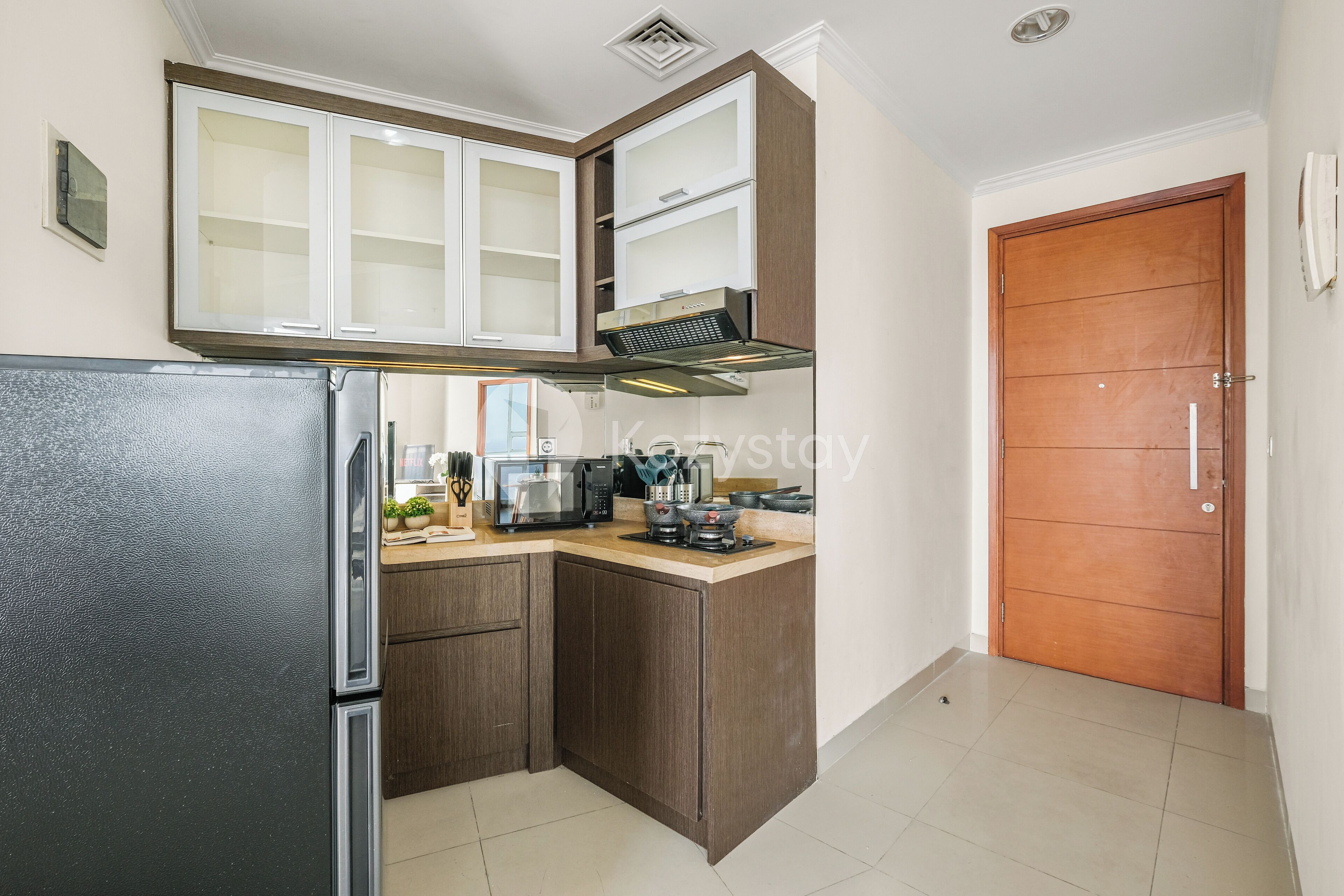 Uma cozinha compacta com geladeira, micro-ondas e fogão. Há um armário de madeira com porta de vidro sobre o fogão.