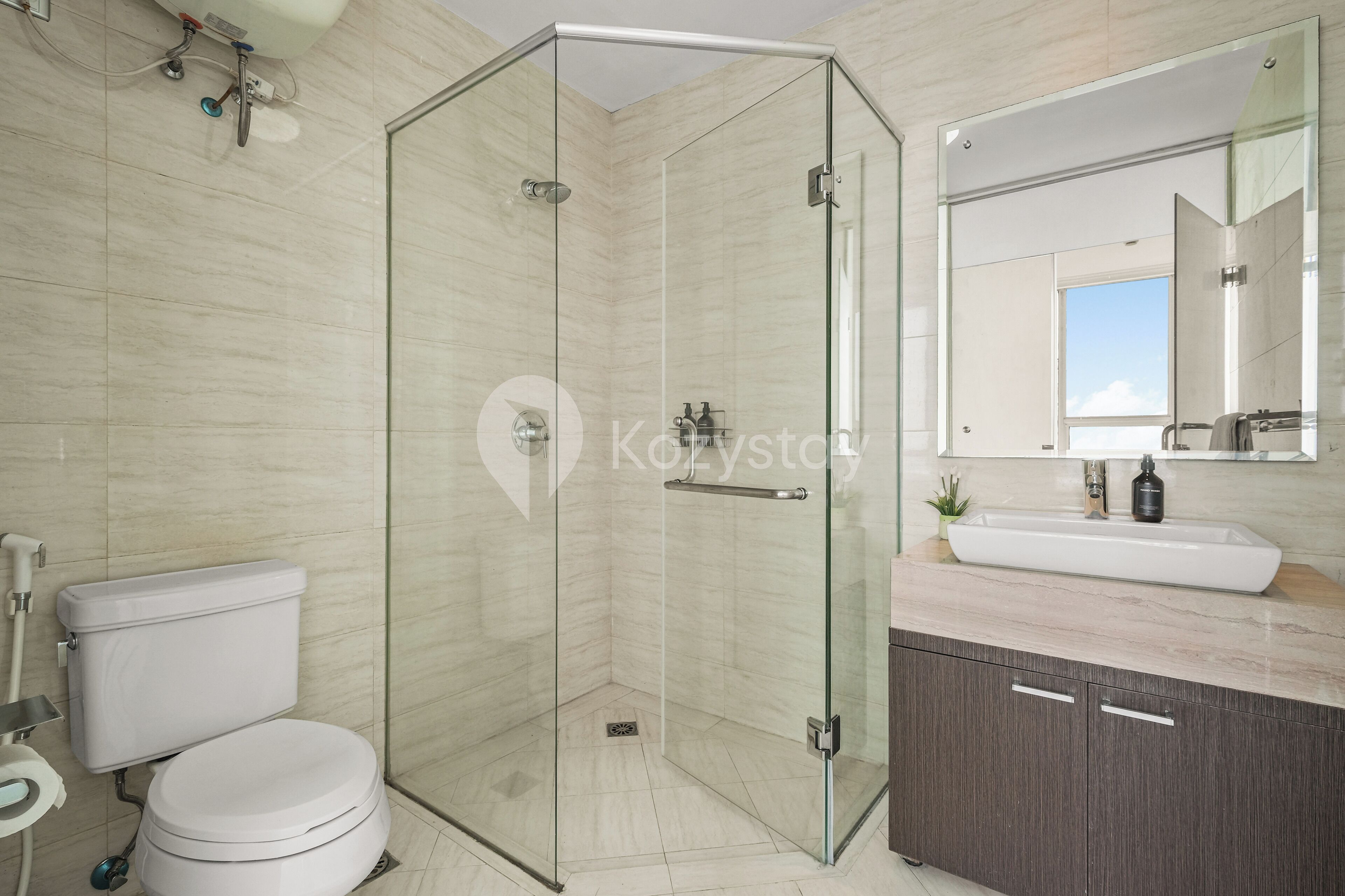 Une salle de bain moderne avec une douche à parois de verre, des toilettes blanches, un lavabo doté d’un plan de travail en marbre et un grand miroir au-dessus du lavabo.