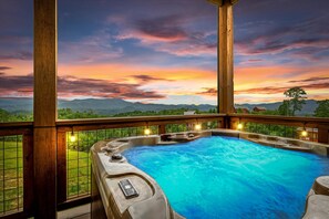 A hot tub with a wooden deck and a view of mountains during sunset.