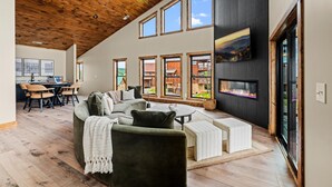 A spacious living area with a high ceiling, large windows, a fireplace, and a dining area with a table and chairs. - Cabin w/ EV Charger, Game Loft & Hot Tub (Sevierville)