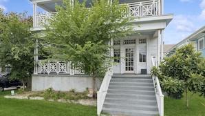 A two-story house with a front porch, a staircase leading to the entrance, and a small garden area. - Fully Furnished 2bd/1.5ba One Block from Carrolton (New Orleans)