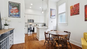 A modern kitchen with white cabinets, a central island, and a dining table with chairs. - Fully Furnished 2bd/1.5ba One Block from Carrolton (New Orleans)