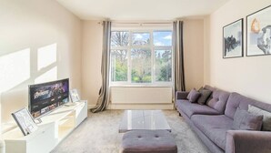 Ein Wohnzimmer mit Flachbildfernseher, einer Couch, einem Couchtisch und einem Fenster mit Vorhängen.