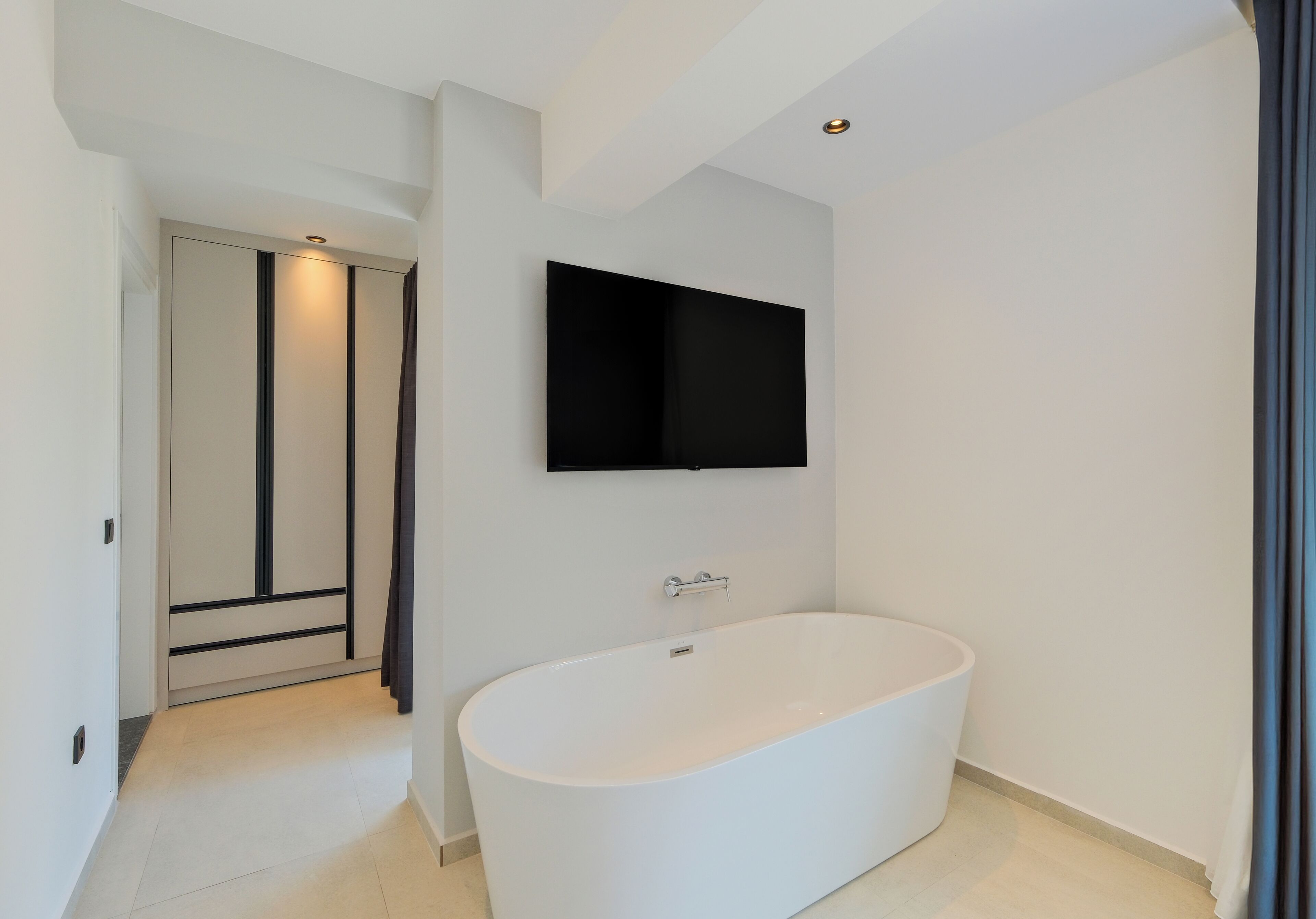 A modern bathroom with a freestanding bathtub, a mounted mirror, and a door leading to another room.