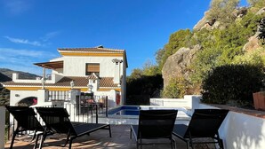 A pool area with black lounge chairs, a white building with a tiled roof, and a view of a mountain in the background. - Spanish country house. Completely free, yet two restaurants within walking distance. (COMARES)
