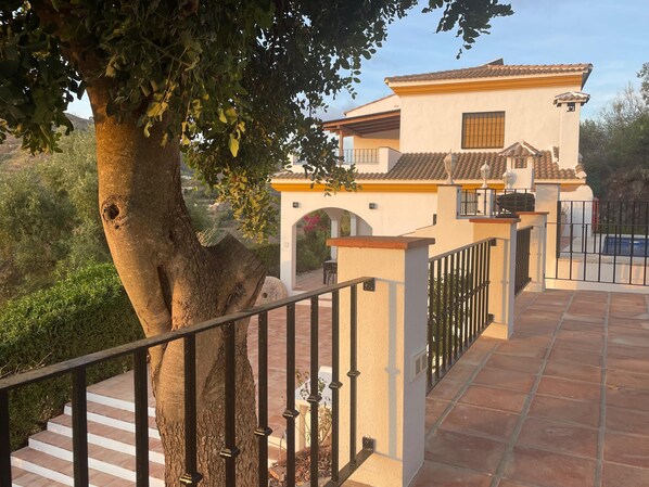 Una villa con techo de tejas, entrada protegida por una reja y una escalera que conduce a la puerta principal.