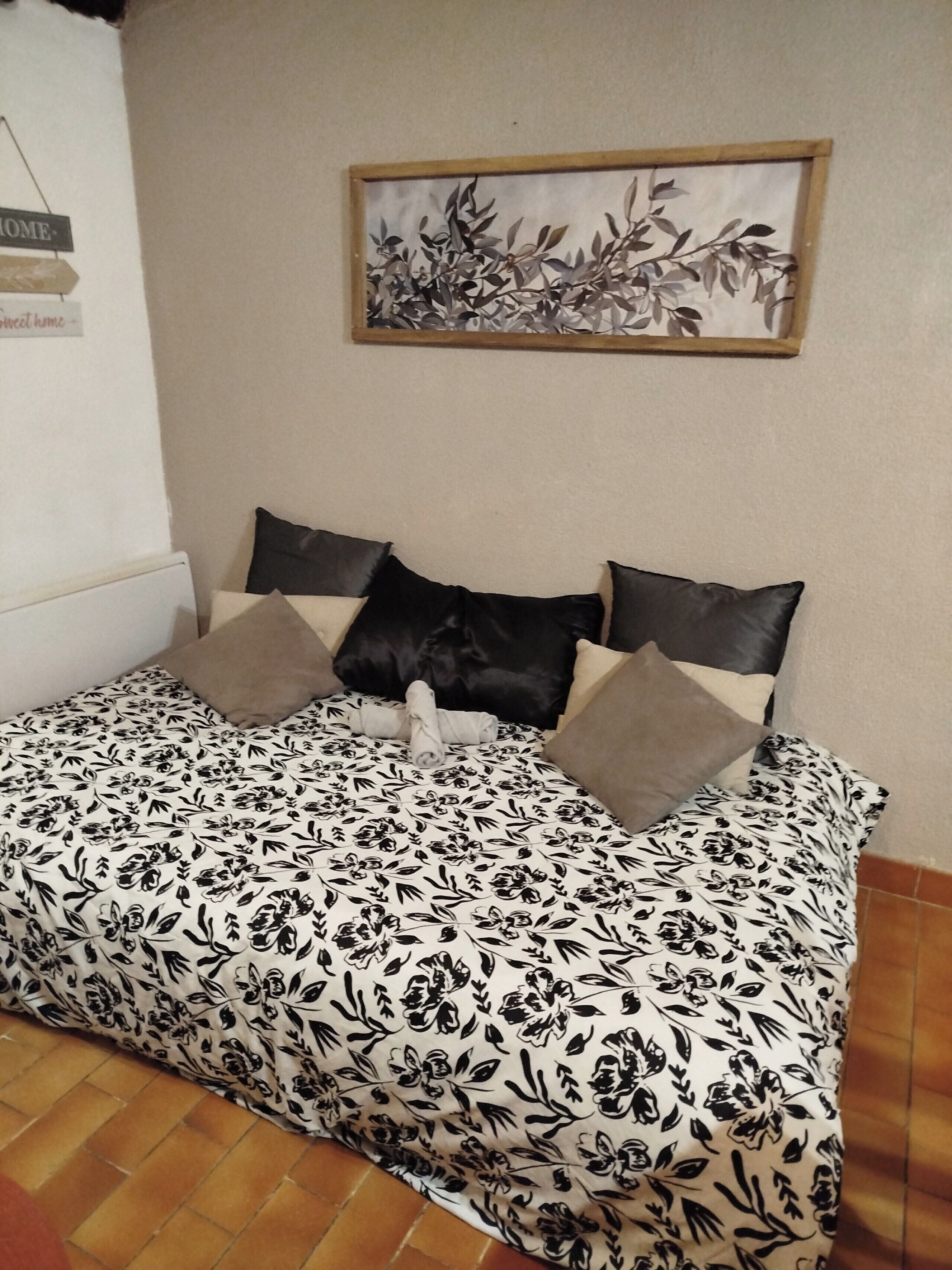 Une chambre à coucher avec un lit, des oreillers, un tableau accroché au mur et une pancarte indiquant « MAISON ».