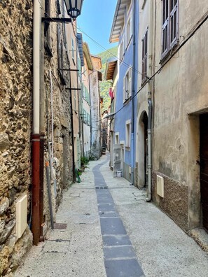 A narrow street with buildings on either side, a paved path, and visible pipes. - Authentic Charming Studio (Breil-sur-Roya)