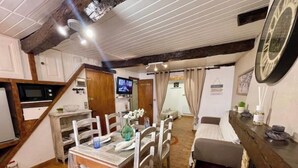 Uma área de refeições acolhedora com mesa e cadeiras de madeira, cozinha com micro-ondas e escada que dá para outro quarto.