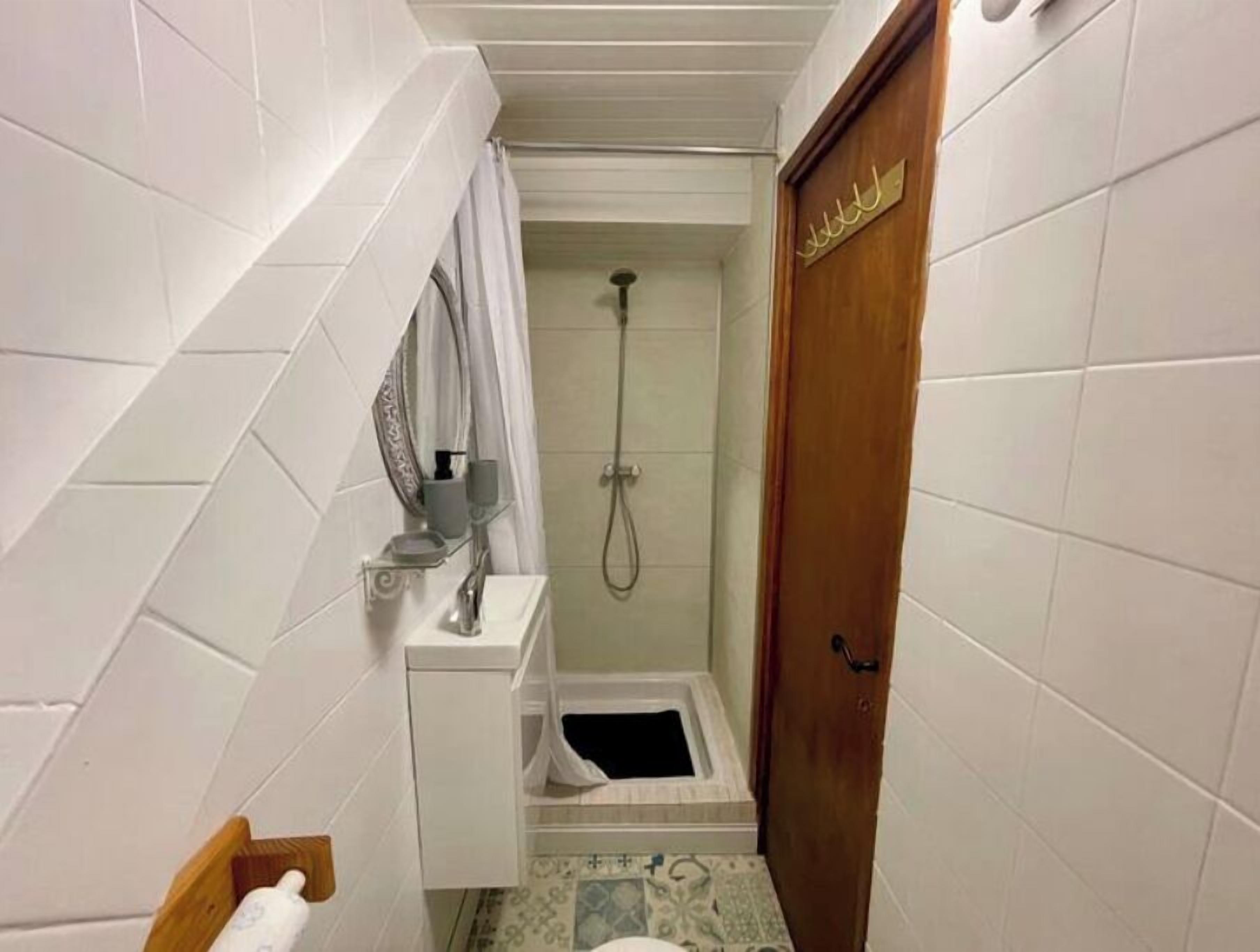 Un baño pequeño y estrecho con azulejos blancos, una ducha, un inodoro y una puerta de madera con un letrero.