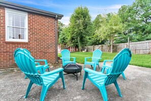 Eine Terrasse mit vier türkisfarbenen Adirondack-Stühlen, die um eine schwarze Feuerstelle angeordnet sind.