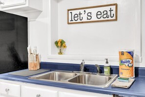 Une cuisine équipée d’un évier à deux bacs, d’un bloc à couteaux, d’un vase avec des fleurs et d’une pancarte sur laquelle on peut lire : « à table ! ».