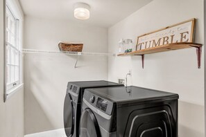 Une buanderie équipée de deux lave-linge à chargement frontal, d’une étagère sur laquelle est posé un panneau indiquant « SÉCHAGE » et d’un panier sur une étagère en fil de fer.