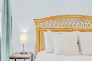 A bed with a wooden headboard and white pillows, a bedside table with a lamp, and a window with curtains.