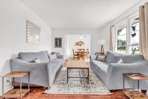 Ein modernes Wohnzimmer mit zwei grauen Sofas, einem Holztisch und einem Essbereich mit Tisch und Stühlen.