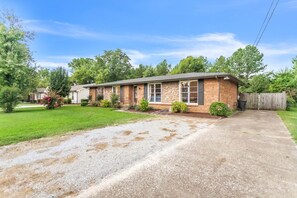 A single-story brick house with a front porch, a driveway, and a wooden fence.