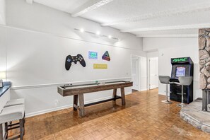 A room with a pool table, a gaming area with arcade machines, and a stone fireplace.