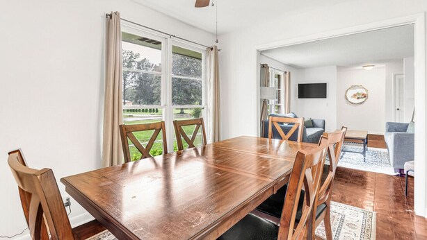 Un comedor con una mesa y sillas de madera, un ventilador de techo y ventanas grandes con cortinas.
