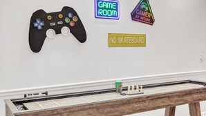 Quarto com um letreiro de neon que diz "GAME ROOM" e outro letreiro com a frase "GAMER AT WORK". Há também uma placa que diz "PROIBIDO PATINS".