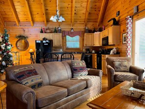 A cozy cabin interior with a leather sofa, a dining table, and a kitchen area. - King Bed, Game Tables, Resort Pools, Putt-Putt, Great Location! (Sevierville)