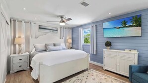 Une chambre à coucher avec un lit, des tables de chevet, un ventilateur de plafond, une télévision et une vue sur la plage.