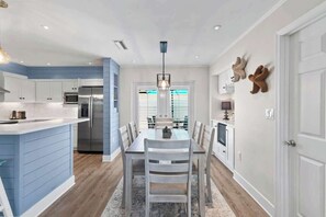Une cuisine moderne avec un mur d’accent bleu, des appareils en acier inoxydable et un coin repas comprenant une table et des chaises en bois.