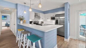 Une cuisine moderne avec un mur d’accent bleu, des meubles blancs et un îlot central doté de tabourets.