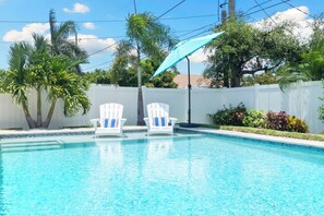 Une piscine avec deux chaises longues blanches et un parasol bleu.