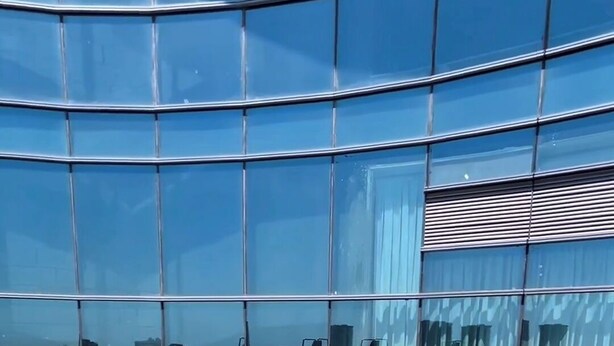 A swimming pool with a tiled edge and metal railings, surrounded by a wooden deck and glass walls reflecting the sky.