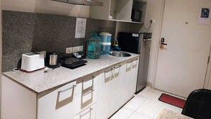 A compact kitchen with a granite countertop, a toaster, a kettle, a water dispenser, and a microwave. There are cabinets below the countertop and a door to the right.