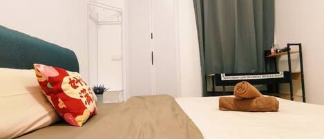 A hotel room with a bed, a desk, a chair, a window with curtains, and a door.