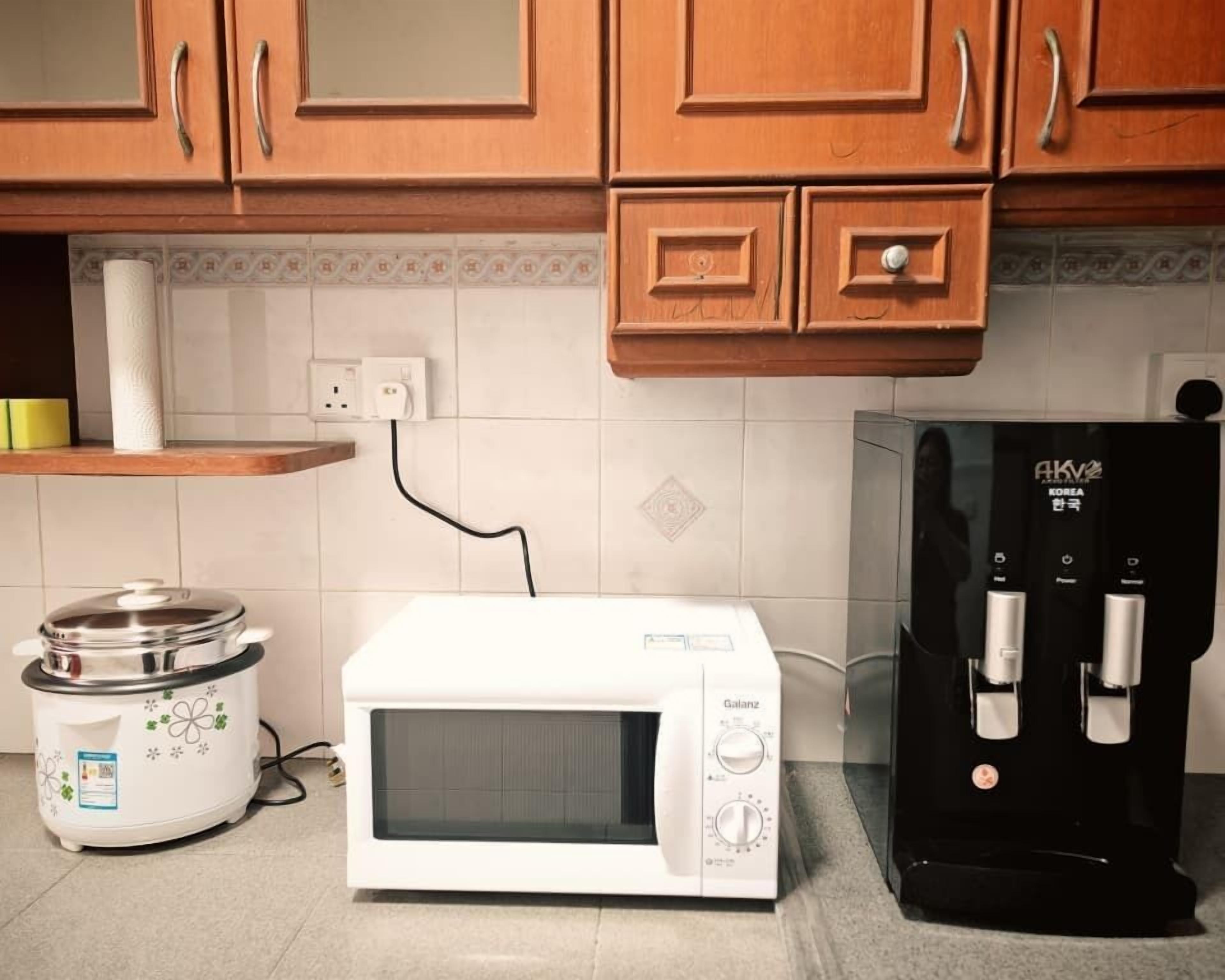 A kitchen with wooden cabinets, a white microwave, a black coffee machine, and a slow cooker.