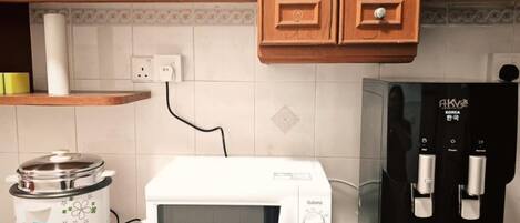 A kitchen with wooden cabinets, a white microwave, a black coffee machine, and a slow cooker.
