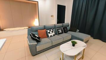 Ein modernes Wohnzimmer mit einem grauen Ecksofa, einem weißen Couchtisch und einem großen Fenster mit Vorhängen.