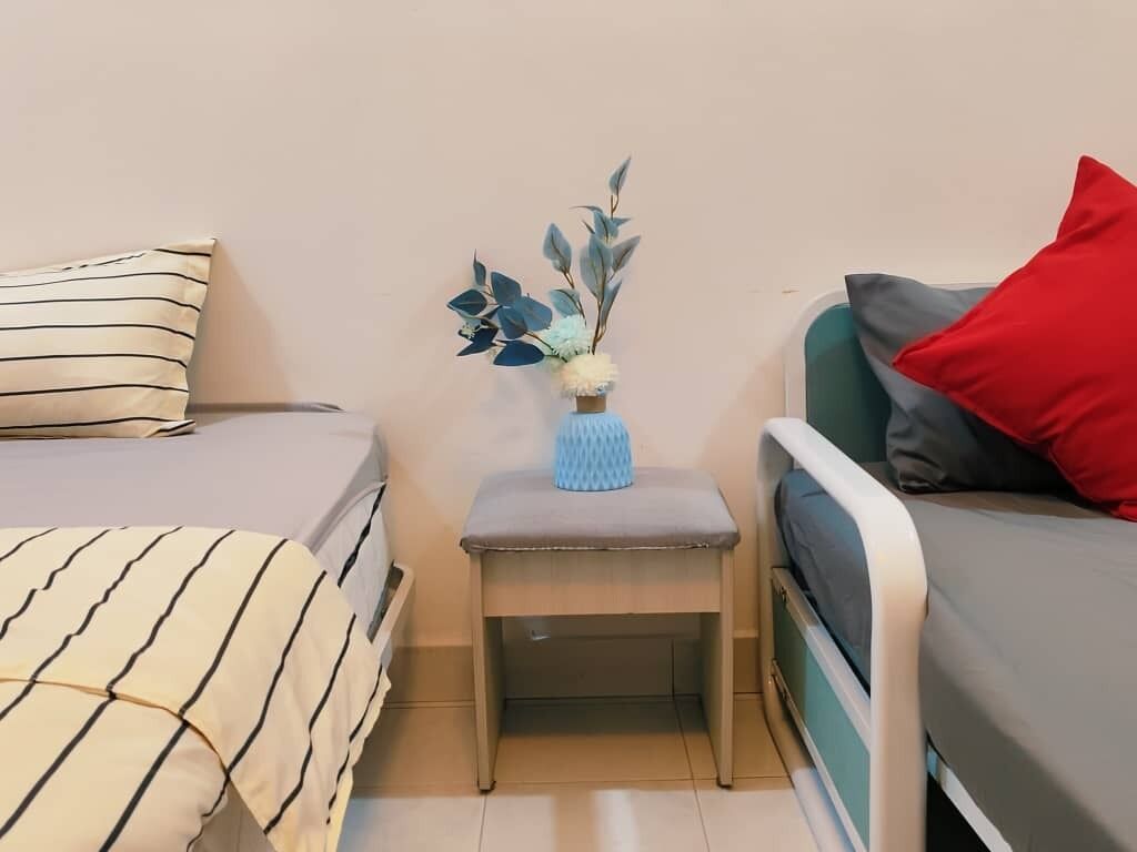 Een slaapkamer met twee bedden, een nachtkastje met een bloevas, en een rode kussen op een bed.