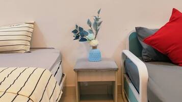 Een slaapkamer met twee bedden, een nachtkastje met een bloevas, en een rode kussen op een bed.