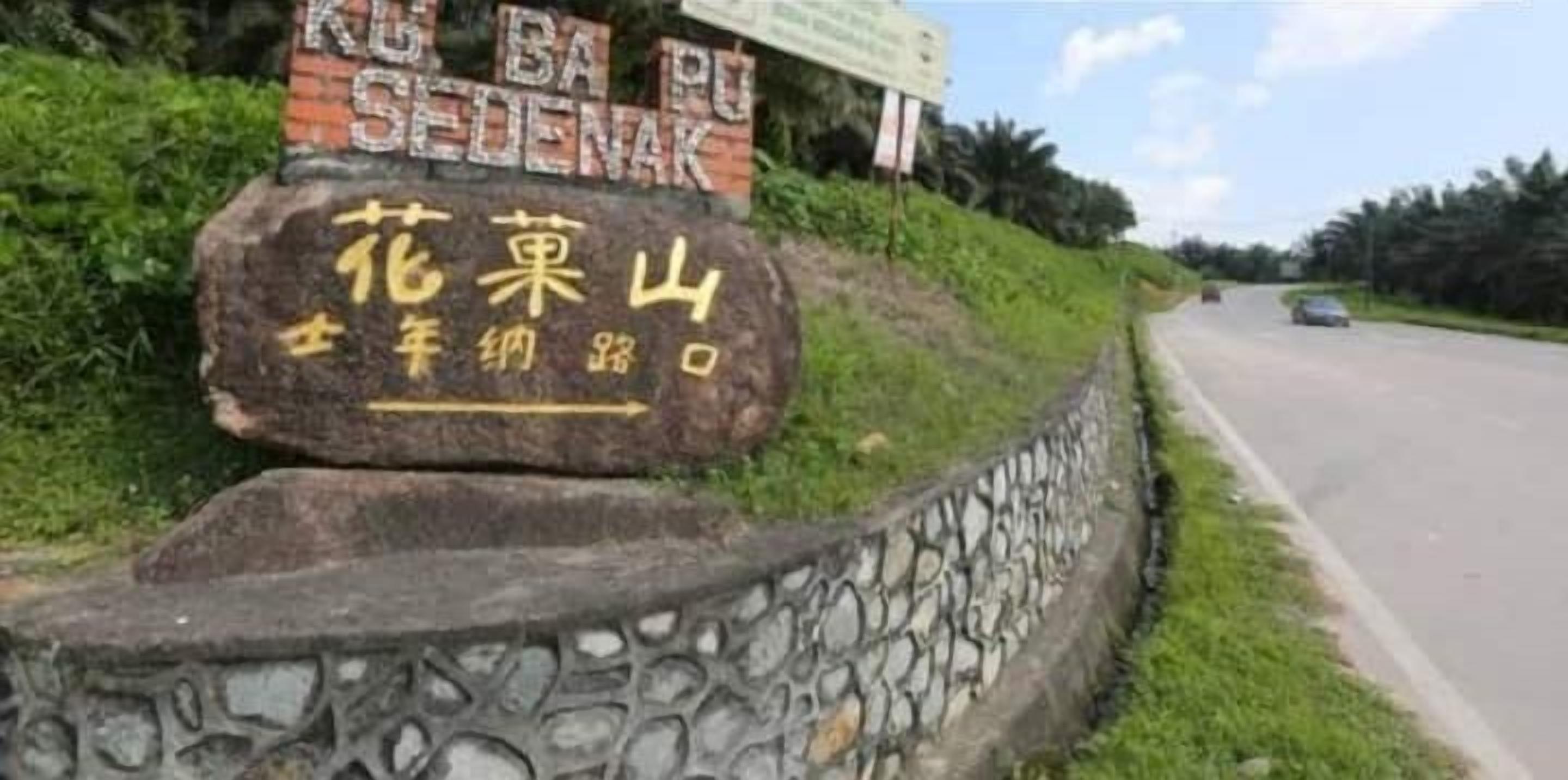 A sign for Hua Guo Shan Temple with a stone wall and a road in the background.