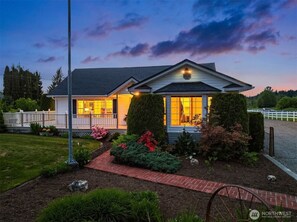 A two-story house with a porch, a well-maintained garden, and a clear sky at dusk.