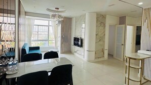 A modern dining area with a large table and chairs, a television mounted on the wall, and a view of the outdoors through large windows. - Sky Garden 3 (Ho Chi Minh City)