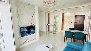 A modern living room with a blue sofa, a small white table, and a large TV mounted on a marble wall. - Sky Garden 3 (Ho Chi Minh City)