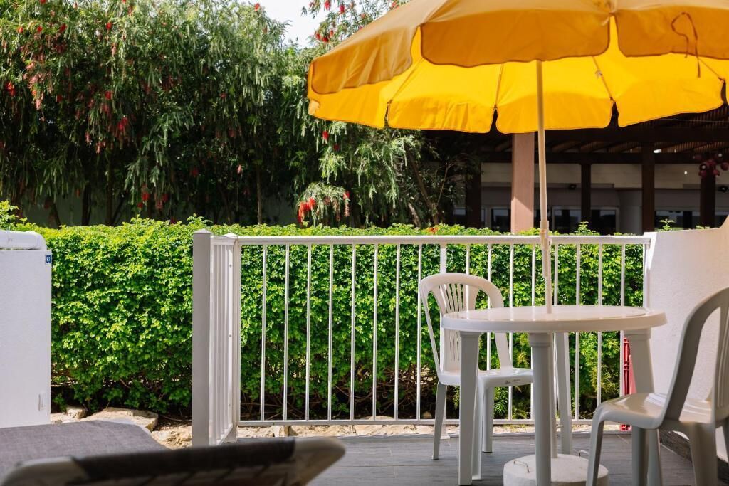 Ein Balkon mit einem gelben Sonnenschirm, weißen Stühlen und einem weißen Tisch.