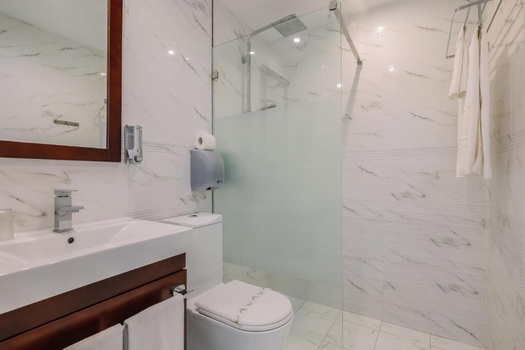 Et moderne badeværelse med et marmorvaskebord, en brusekabine i glas og et hvidt toilet.