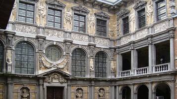Un bâtiment historique à l’architecture classique, caractérisé par des fenêtres en arc, des sculptures en pierre détaillées et une cour intérieure.