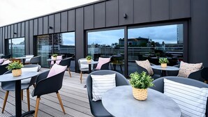 Une terrasse sur le toit dotée d’un mobilier d’extérieur moderne, de grandes fenêtres et de plantes en pot.