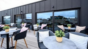 A rooftop terrace with modern outdoor seating, large windows, and potted plants.