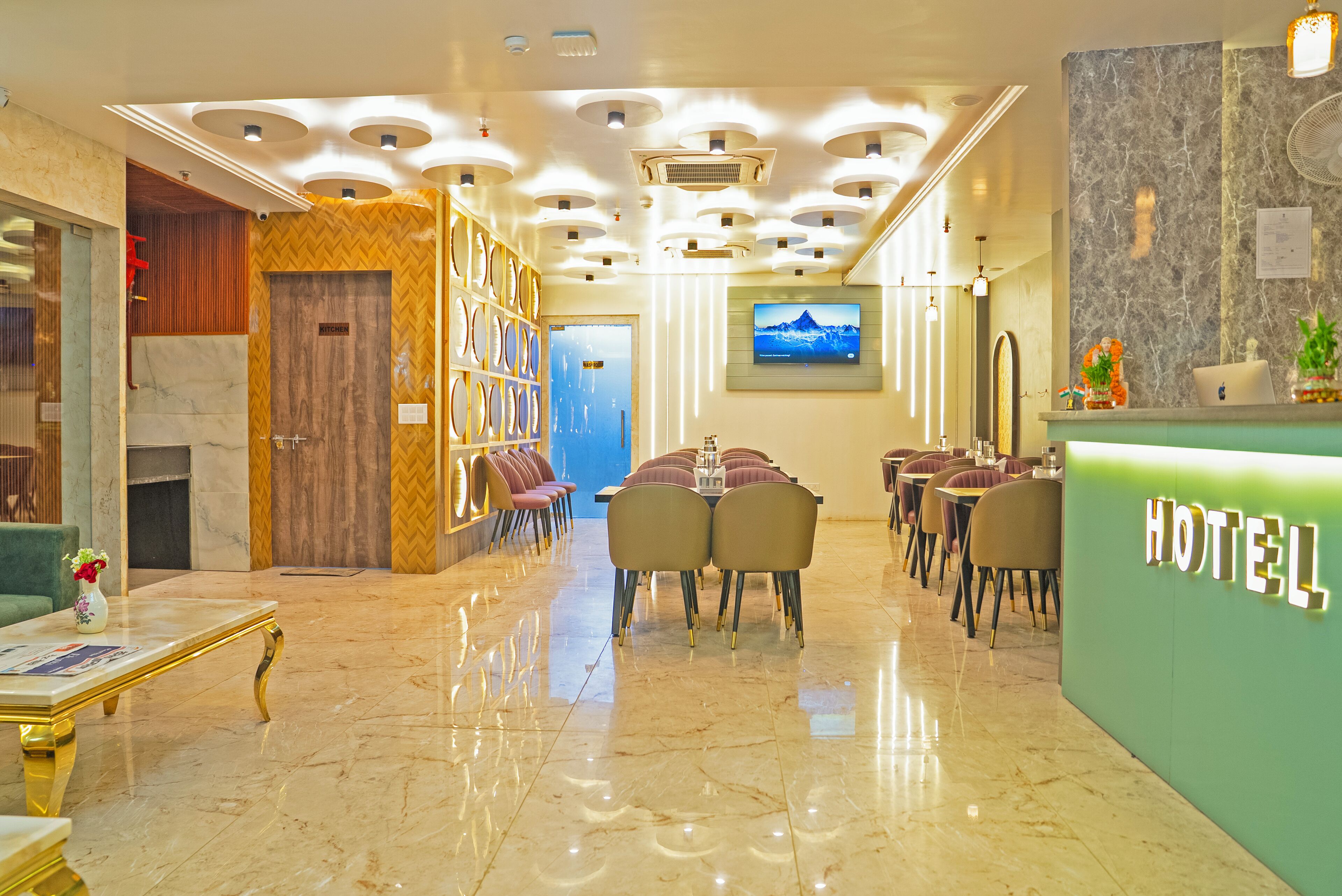 Een hotel lobby met een marmeren vloer, een receptiebalie, een zithoek en een televisiescherm waarop een uitzicht op bergen te zien is.