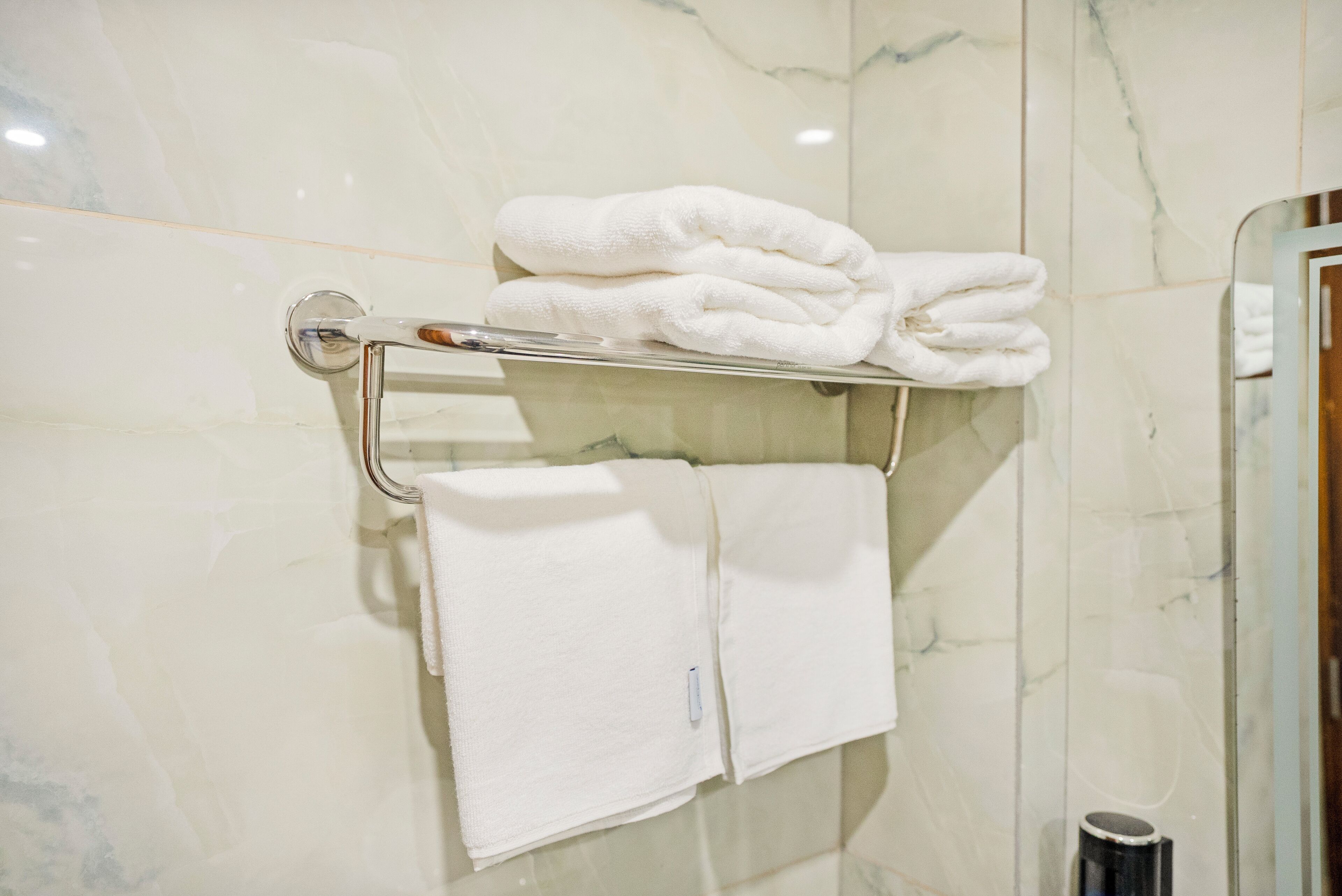 Een badkamer met een marmeren wand, een handdoekhouder met opgevouwen handdoeken en een handdroger.